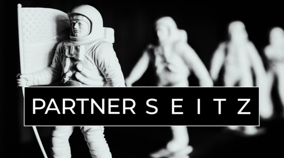 Schwarz weißes Foto mit weißen Astronauten Figuren Die in einer Reihe stehen und nach hinten unscharf werden Punkt Die erste Figur trägt eine Flagge. Über dem Foto ist das Firmenlogo in Schwarz/weiß mit dem Schriftzug PartnerSeitz