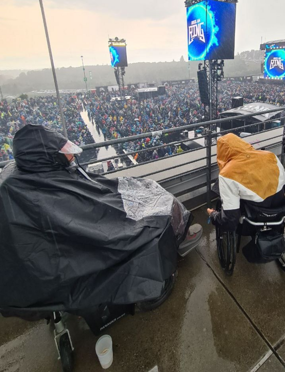 Ein E rolli fahrer steht bei Rock am Ring auf der Rollstuhltribüne im strömenden Regen und trägt ein Regencape