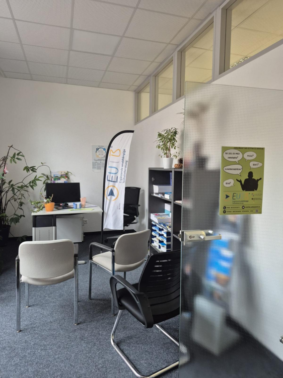 Das Bild zeigt einen Beratungsraum mit drei Stühlen und einem Schreibtisch, auf dem ein PC Monitor steht